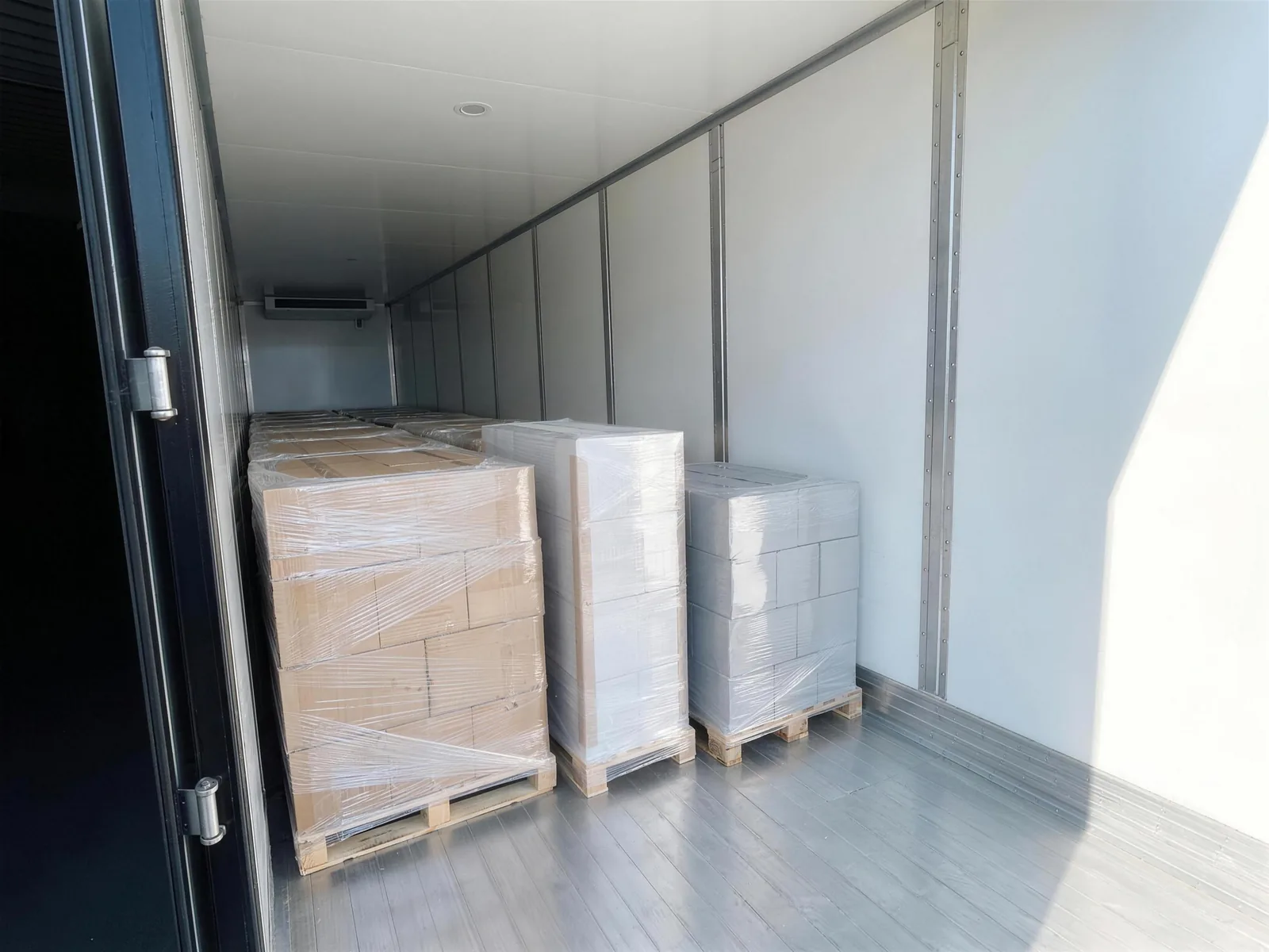 Separately wrapped pallet shipments from different shippers lined along one trailer wall, seen from just inside the open doorway