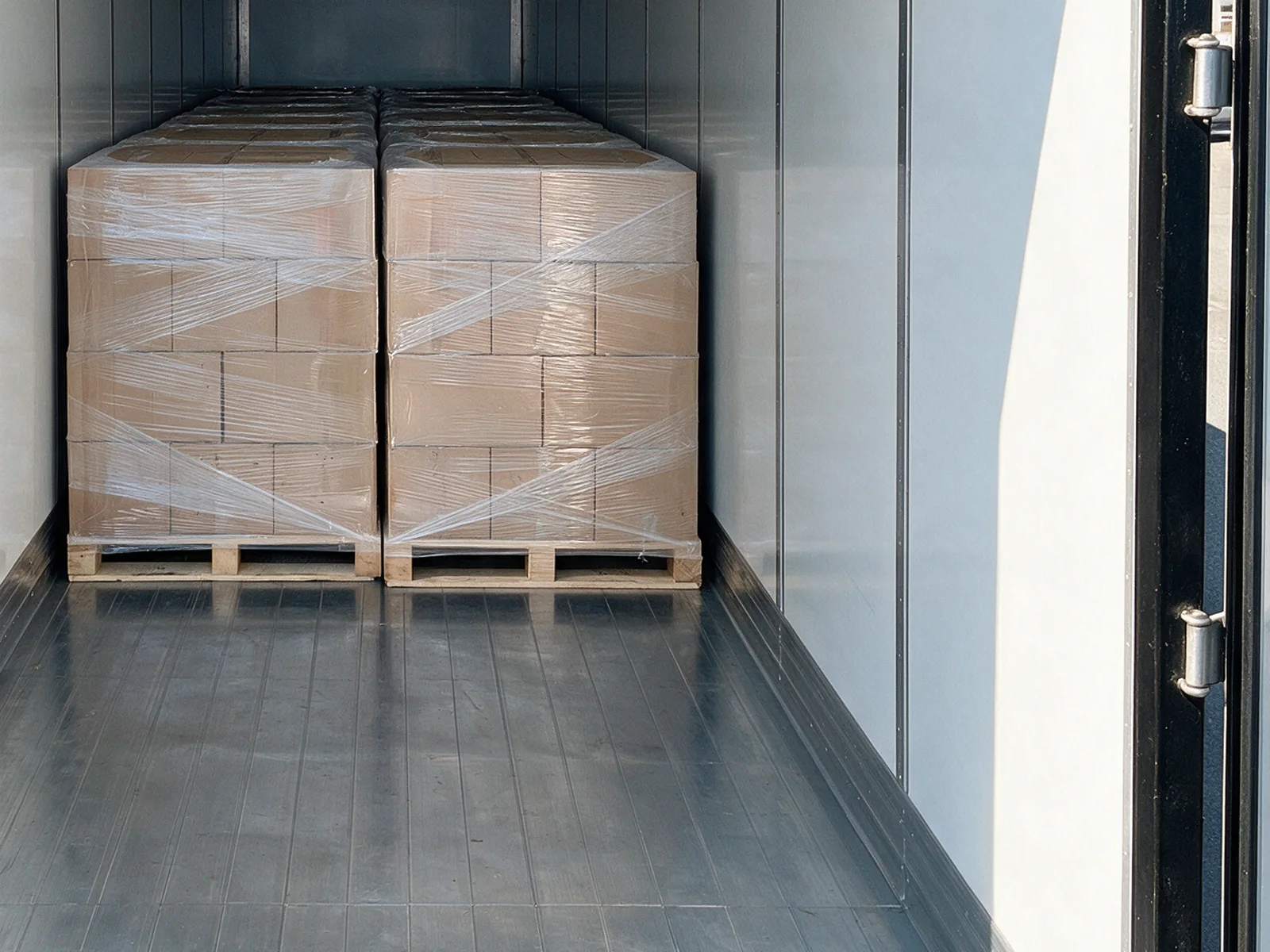 A partial load of wrapped pallets set at one side of the trailer, with the open deck sweeping away beside it